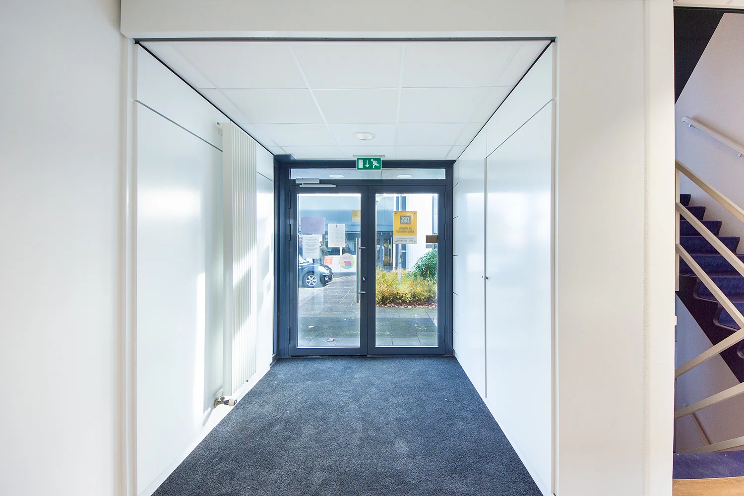 Verlichte gang met tapijtvloer en glazen deur naar buiten aan de Huis-ter-Heideweg.